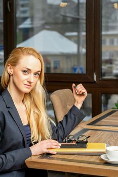 Portrait of a young caucasian businesswoman with documents and laptop at the table looking at the camera in cafe