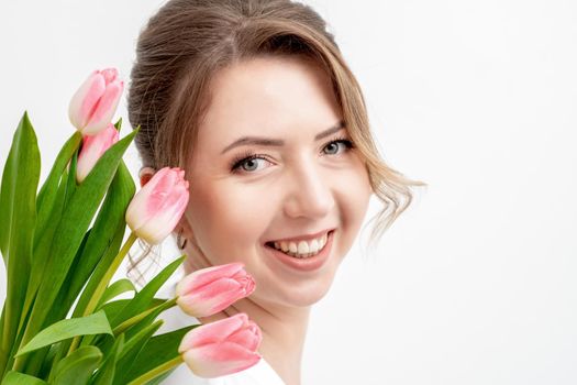 Portrait of a happy young caucasian woman with pink tulips against a white background