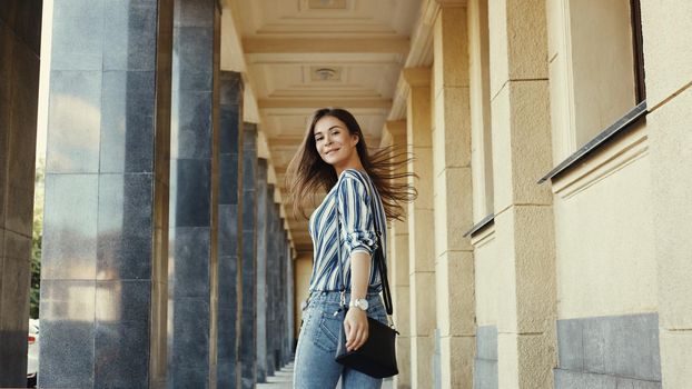 Street Style Outdoors Portrait of Beautiful Girl. Young Woman Smiling. She wearing Print Shirt, Blue Jeans and Black Bag. Happy Lifestyle shoot