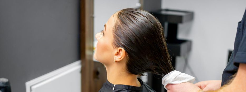 The hairdresser dries the washed hair with a towel to a beautiful young brunette woman at a beauty salon