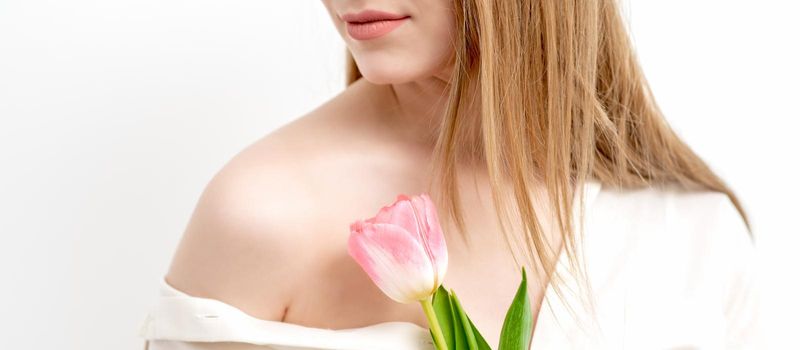 Half face portrait of a beautiful young caucasian woman with one pink tulip on white background