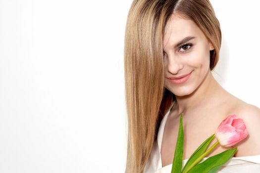 Portrait of a happy young caucasian woman with one pink tulip against a white background with copy space