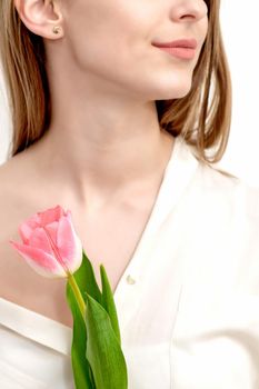Half face portrait of a beautiful young caucasian woman with one pink tulip on white background