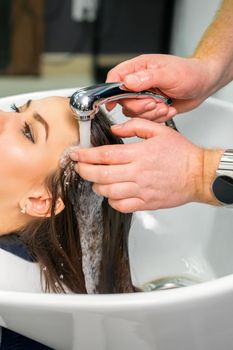 A male hairdresser begins to wash the hair of a young woman in a sink in a hair salon