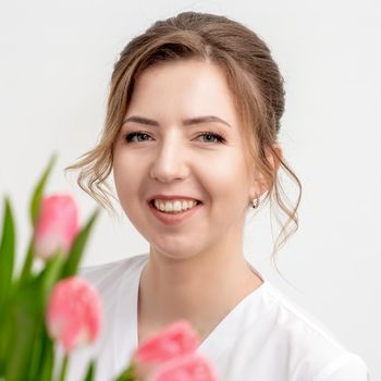 Portrait of a happy young caucasian woman with pink tulips against a white background