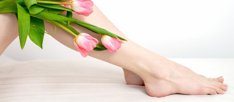 Beautiful slim smooth woman's legs with tulips flowers on white background