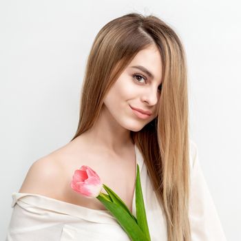 Portrait of a happy young caucasian woman with one pink tulip against a white background with copy space