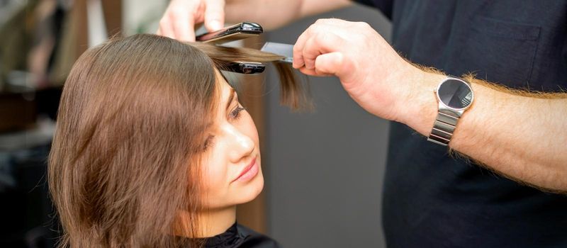 A male hairdresser is straightening the hair of the young woman in a beauty salon