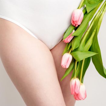 Bikini area of a young woman wearing a white underwear with pink tulips on white background