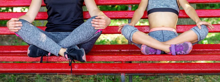 Mother with daughter wearing sportswear sitting on the bench in the summer park