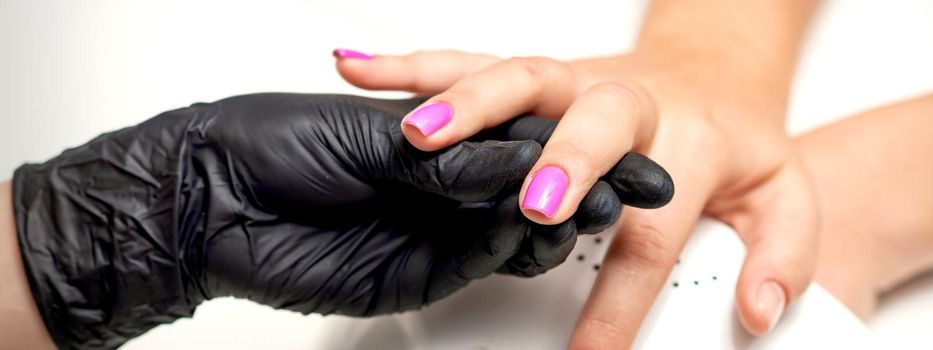 Manicure master's hand holds a female finger with purple nail polish while painting the nails in a nail salon