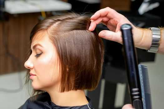 A male hairdresser is straightening the hair of the young woman in a beauty salon