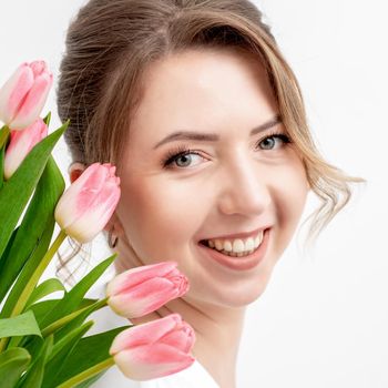 Portrait of a happy young caucasian woman with pink tulips against a white background