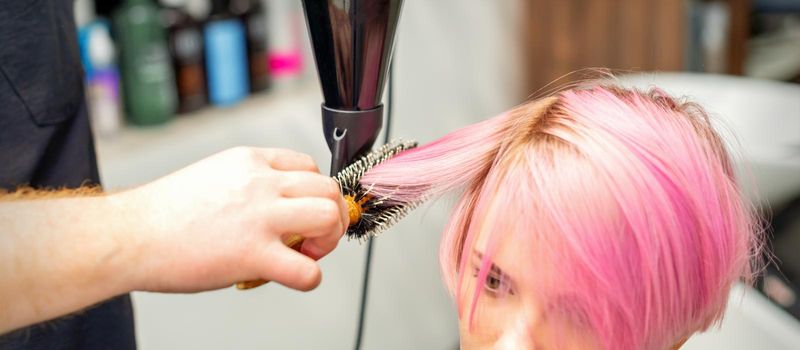 Hairdresser dries pink hair of the young woman in a beauty salon