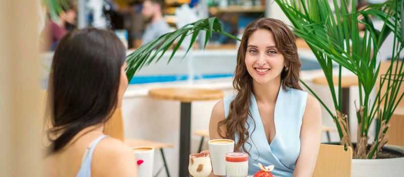 Two beautiful young caucasian women drink coffee sitting at the table in cafe outdoor