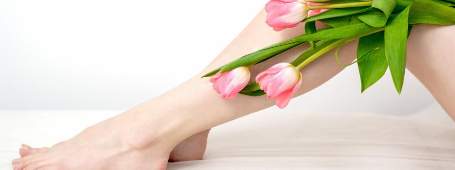 Beautiful slim smooth woman's legs with tulips flowers on white background