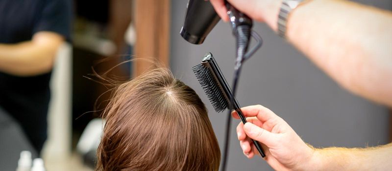 Hairdresser dries brown hair of the young woman in a beauty salon