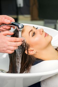 A male hairdresser begins to wash the hair of a young woman in a sink in a hair salon