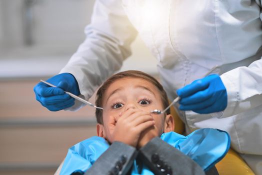 How am I going to get out of this. a frightened little boy lying down on a dentist chair and holds his mouth closed to keep the dentist from working on him