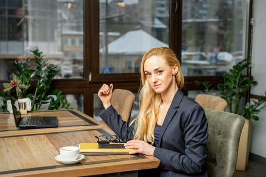 Portrait of a young caucasian businesswoman with documents and laptop at the table looking at the camera in cafe