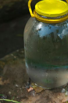 Misted up glass jar full of pure cold spring water standing on the stone near natural water spring, clear drinking water concept.
