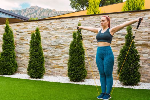 young sportswoman, stretching her body muscles with elastic bands outdoors in the garden of her house. concept of health and well-being. natural light in the garden.