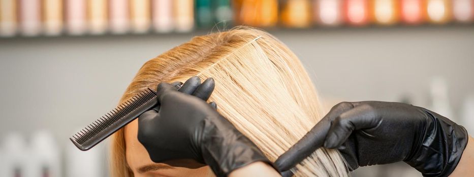 Hairdresser's hand combs female hair before dyeing in a beauty salon