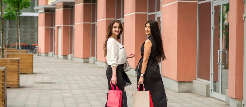 Two beautiful young caucasian happy women with shopping bags walk into the shopping mall