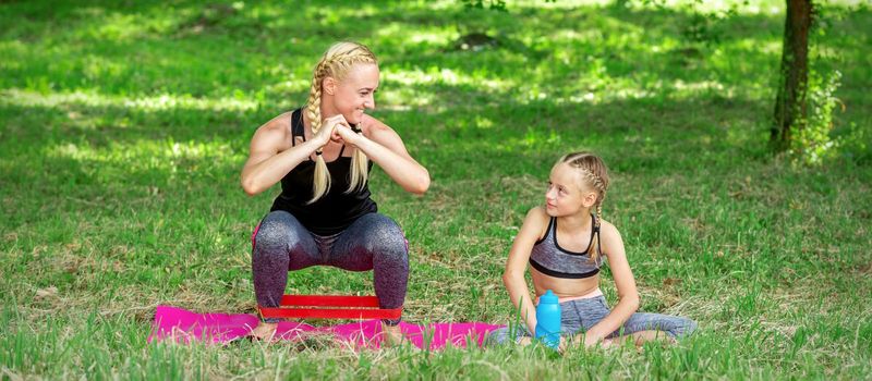 Mother and daughter doing sports exercises on the mat in the park outdoor