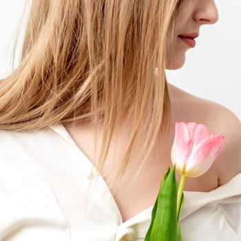 Half face portrait of a beautiful young caucasian woman with one pink tulip on white background
