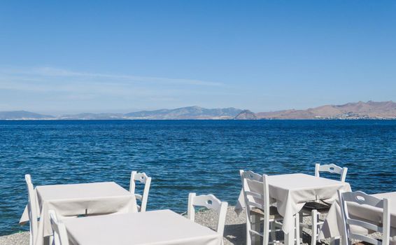 White restaurant tables on the beach in summer - travel, vacation and summer concept. The perfect lunch with a sea view