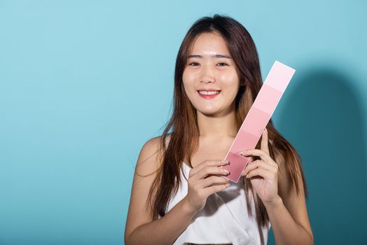 Portrait of happy female hold color card under sun protection, skin beauty face, Asian beautiful young woman smiling and holding skin color scale paper studio shot isolated on blue background