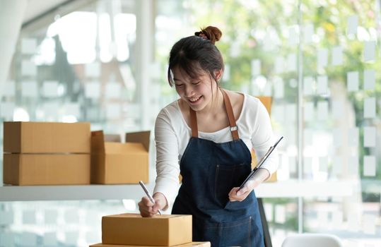 Startup happy Asian woman business owner works with a box at home, prepare parcel delivery SME supply chain, procurement, package box to deliver to customers, Online SME business entrepreneurs ideas,.