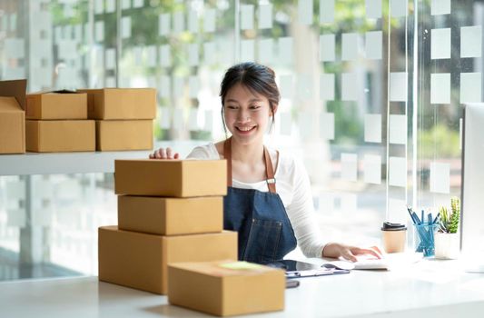 Startup SME small business entrepreneur SME or freelance Asian woman using a laptop with box, Young success Asian woman with her hand lift up, online marketing packaging box and delivery, SME concept..