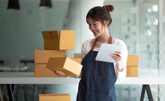 Startup SME small business entrepreneur SME or freelance Asian woman using a laptop with box, Young success Asian woman with her hand lift up, online marketing packaging box and delivery, SME concept..