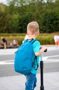 A boy on a scooter along the embankment of the city. Journey. Backpack on the back. The face expresses natural joyful emotions. Not staged photos from life.