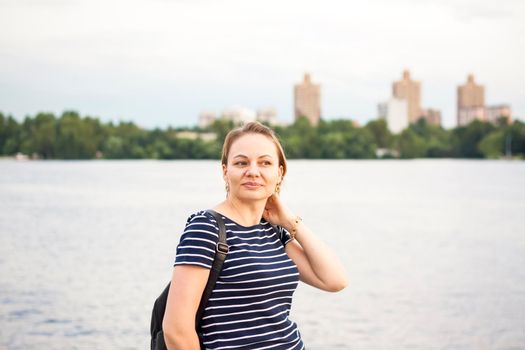 A girl standing on the river embankment straightens her hair with her hand. Evening walk around the city