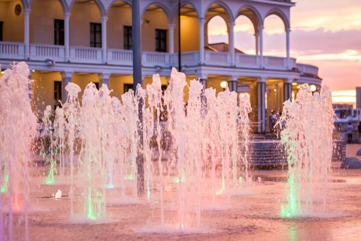 Street fountains near the building in the park in the sunset light. Evening walk around the city