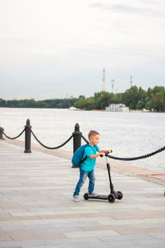 A boy on a scooter along the embankment of the city. Journey. Backpack on the back. The face expresses natural joyful emotions. Not staged photos from life.