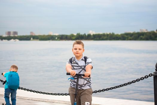 A boy on a scooter along the embankment of the city. Journey. Backpack on the back. The face expresses natural joyful emotions. Not staged photos from life.