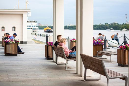 2022-07-17. Russia. Moscow. Northern River Station. Young people, a couple are sitting on a bench, admiring the view of the river. Other people are resting nearby. Moscow River