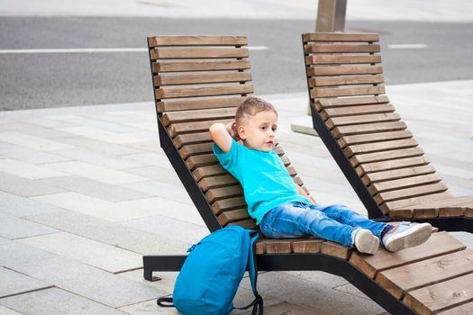 A boy in a blue T-shirt is resting on a chaise longue that stands on the embankment. Journey.  The face expresses natural joyful emotions. Not staged photos from nature.