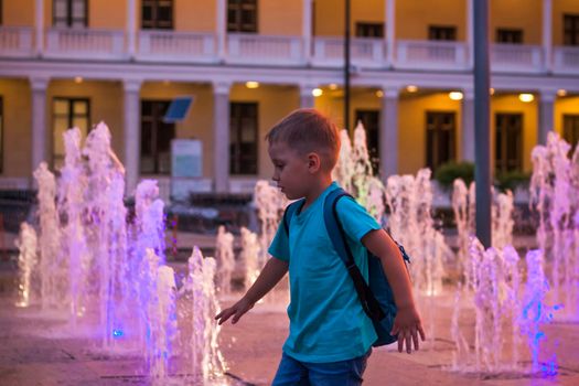 Children have fun frolicking in the fountains near the building in the park in the sunset light. Evening walk around the city