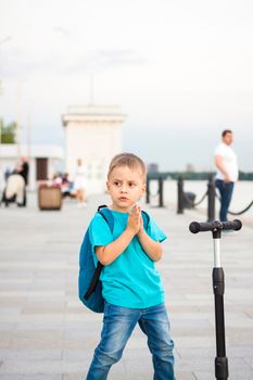 A boy on a scooter along the embankment of the city. Journey. Backpack on the back. The face expresses natural joyful emotions. Not staged photos from life.