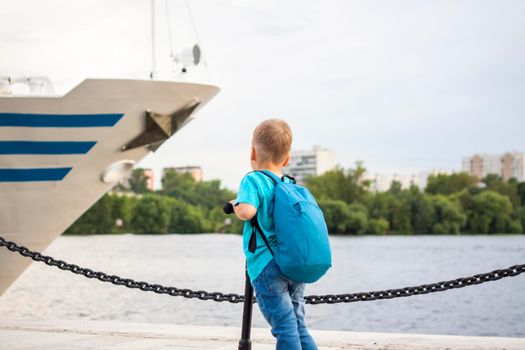 A boy on a scooter along the embankment of the city. Journey. Backpack on the back. The face expresses natural joyful emotions. Not staged photos from life.