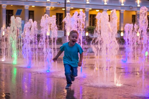 Children have fun frolicking in the fountains near the building in the park in the sunset light. Evening walk around the city