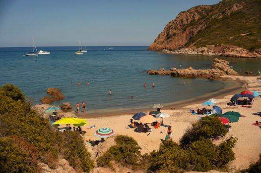 Beach of southern Sardinia (Cala Sa Figu) inserted in a natural bay full of tourists with umbrellas on vacation.