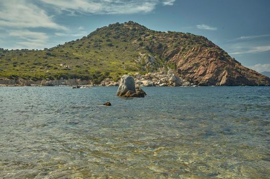 Superb green hill on the sea with a rock in the middle that emerges from the sea itself in the southern coast of Sardinia.