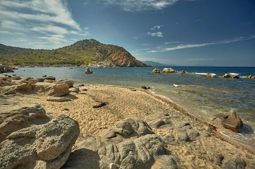 Beautiful Mediterranean beach typical of the coast of southern Sardinia taken over in summer. The beach, the rocks and the mountains behind blend in a wonderful panorama of amazing beauty.