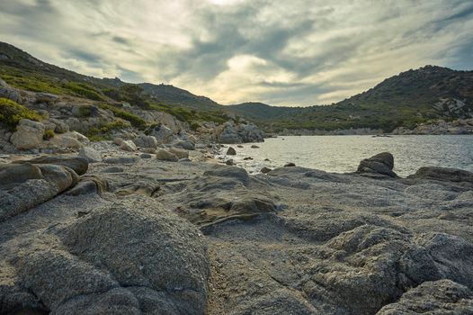 Beautiful Mediterranean beach typical of the coast of southern Sardinia taken over in summer. The beach, the rocks and the mountains behind blend in a wonderful panorama of amazing beauty.